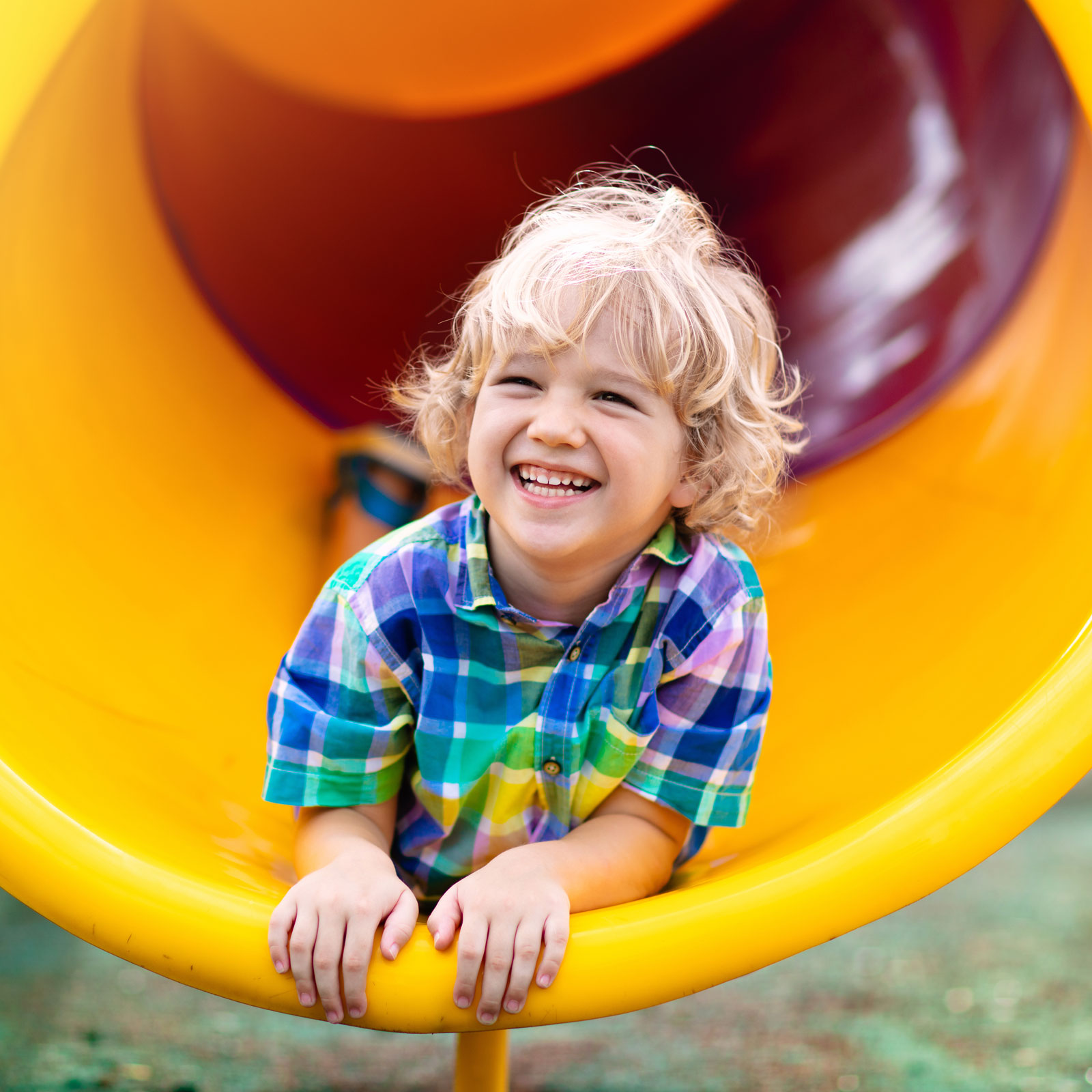 a smiling boy goes down a slide on his belly