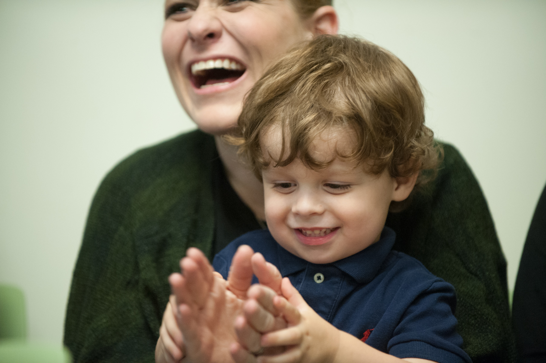 A parent holding a young child who is clapping.